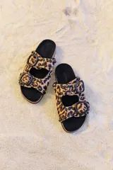 Sandalia tipo birkenstock de pelo con estampado animal print (leopardo), con dos tiras ajustables y tachas metálicas negras. La plantilla es de corcho y la suela de goma eva.