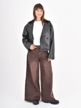 Jean de corte wide leg en color óxido con efecto lavado. Presenta una abertura lateral decorada con pequeñas tachas metálicas a lo largo de toda la pierna.
