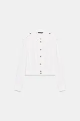 Camisa corta de cuello solapa y manga larga, con trabillas decorativas en los hombros. Presenta pliegues delanteros, elástico en la espalda y cierre frontal con botones.