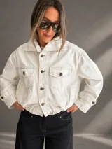Campera bomber de denim blanco, confeccionada en mezcla de algodón y poliéster, con silueta relajada y largo a la cintura. Cuenta con cuello amplio, bolsillos delanteros con solapa, cierre frontal con botones y cintura elastizada.