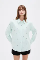 Blusa de corte holgado con cuello camisero y cierre frontal de botones. Presenta un diseño de rayas verticales finas en color azul y blanco, decorado con pequeños bordados dispersos.