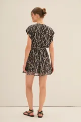 Vestido corto con escote en V profundo y mangas cortas estilo kimono. Presenta un estampado floral con hilos metalizados dorados sobre fondo negro y un ruedo con volado. Incluye forro interior.