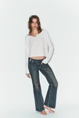Jeans de tiro bajo con corte bootcut, confeccionados en denim con efecto lavado. Presentan costuras verticales marcadas en el frente, cierre frontal con cremallera, gancho metálico y detalle de trabilla con botones en la cintura.