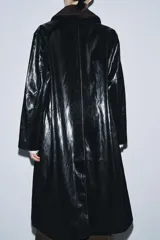 Trench de largo midi con acabado brillante efecto vinilo, manga larga y cuello de solapa en tejido de gamuza a contraste. Presenta cierre frontal con botones ocultos y bolsillos laterales integrados en la costura.