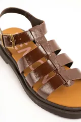 Sandalias cangrejeras de cuero marrón charol, estilo romano con múltiples tiras cruzadas, suela track plana y cierre de hebilla metálica ajustable en el tobillo.