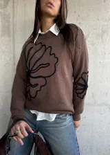 Sweater de punto color chocolate con diseño de flores bordadas en hilo negro en el frente y en una de las mangas. Presenta cuello redondo y puños acanalados.