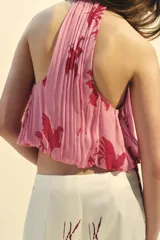 Top sin mangas color rosa con estampado de flores rojas, cuello halter y espalda descubierta.