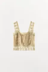 Top de estilo corset confeccionado en viscosa satinada color beige. Presenta escote recto, tirantes anchos con terminación de encaje, detalle de pliegues verticales, lazada frontal y aplicaciones de encaje con bordados florales en el cuerpo y el ruedo.