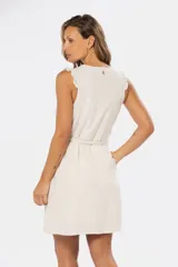 Vestido corto sin mangas color beige claro, con escote en V, botones frontales de madera y cinturón de lazo a juego. Presenta pequeños volados en los hombros y bolsillos laterales.