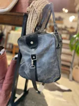 Bolso de viaje tipo duffel de cuero negro con detalles de refuerzo en gamuza y doble asa de mano.