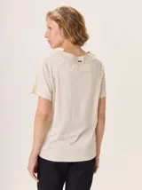 Remera negra de manga corta con escote en V y cuello redondo abierto. El cuerpo de la prenda tiene un acabado brillante o con lurex, mientras que el cuello es de un material liso y opaco.