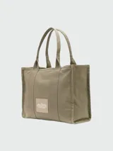 Bolso tipo tote de Marc Jacobs, confeccionado en lona resistente de color negro. Presenta el nombre del modelo estampado en blanco en la parte frontal y el logo de la marca debajo. Cuenta con doble asa superior para llevar al hombro o en la mano.