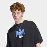 Remera Adidas de algodón color negro, con ajuste holgado, cuello redondo y moldería clásica de manga corta. Presenta un estampado gráfico frontal inspirado en el logo Trefoil con un diseño de personaje estilizado en tonos azules y blancos.