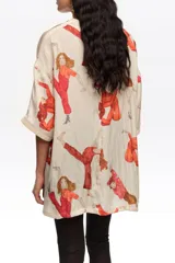 Blusa de corte oversize color beige, con estampado artístico de personas en movimiento de tonos rojos, escote en V y mangas cortas.