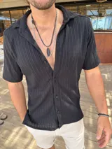 Camisa de tejido texturizado color negro, con cuello solapa, manga corta y cierre frontal de botones.