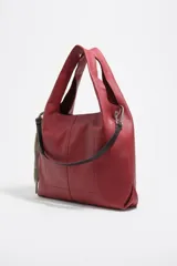 Bolso de mano grande Bimba y Lola modelo Paper, confeccionado en piel vacuna de color rojo. Presenta estructura blanda, asas de hombro fijas, tira lateral con mosquetón y detalle de logo metálico en la parte inferior.