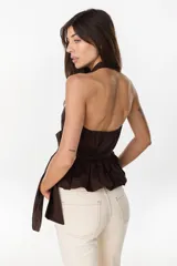 Blusa de cuello halter en color beige, con escote en V pronunciado, corte ajustado en el torso y detalle de volados fruncidos en la cintura con un lazo lateral ajustable.