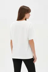 Remera blanca de algodón de manga corta, con cuello redondo y corte holgado. Presenta estampado frontal de un lazo con detalles de brillos y la frase 'Made of sweetness'.