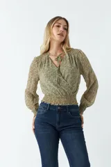 Blusa de manga larga con estampado floral pequeño sobre fondo oscuro. Presenta escote en V con lazo para anudar, cintura con frunce elástico y puños ajustados.