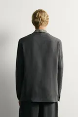 Blazer relaxed fit de color negro, confeccionada en tejido fluido con mezcla de viscosa y lino. Presenta cuello sin solapas, manga larga, bolsillos de solapa en la cadera y cierre frontal de un botón.