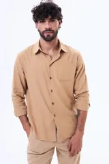 Camisa de manga larga en color beige, con cuello clásico, cierre frontal de botones y un bolsillo aplicado en el pecho. Presenta un corte relajado y tela liviana.