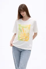 Remera de algodón color blanco, de corte holgado y manga corta, con cuello a la base. Presenta un estampado frontal rectangular en tonos amarillos y verdes con motivos botánicos, realzado con detalles bordados y lentejuelas.