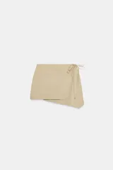 Falda mini de tiro medio en color beige, con diseño cruzado y bajo asimétrico. Presenta un cierre lateral con lazada ajustable.