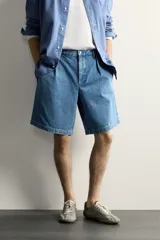 Bermuda de denim con corte relaxed fit, tiro medio y pierna recta. Presenta pliegues frontales dobles, bolsillos laterales y bolsillos traseros de doble vivo. Confeccionada en tejido rígido con efecto lavado, cierre frontal con cremallera y botón.