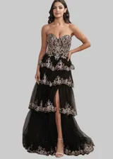 Vestido largo de fiesta con escote corazón y corset estructurado. Presenta un diseño de capas de tul con volados y bordados brillantes en tonos dorados sobre base negra. Incluye un tajo lateral profundo en la falda.