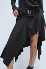Vestido midi de cuello redondo y manga larga, confeccionado en tejido de punto gris oscuro. Presenta un cinturón integrado con hebilla y aplicación de tachas metálicas, y un bajo con diseño asimétrico y volados.