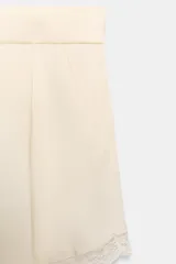 Shorts de tiro medio confeccionado en tejido satinado, con pinzas en el delantero, bolsillos laterales y detalle de encaje a tono en el ruedo. Cuenta con cierre frontal mediante cremallera, botón interior y gancho metálico.