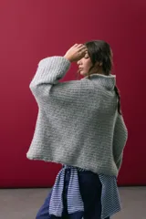 Buzo tejido en mohair de color gris, con silueta amplia y corte en línea A. Presenta cuello tipo remera con broches que permiten cerrarlo como polera, mangas largas con puños y un diseño de tejido horizontal.