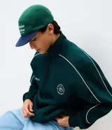 Buzo de cuello alto con medio cierre frontal, confeccionado en tejido de algodón con felpa. Presenta un corte boxy holgado, mangas largas con puños elásticos y una estampa gráfica circular en la espalda con la inscripción Off-Track Studio Company.