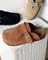 Zueco de cuero vacuno con diseño de punta redonda, ajuste mediante correa con hebilla metálica y suela de corcho con base de goma antideslizante.