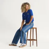 Pantalón Adidas Firebird de denim azul de corte holgado, con tiro medio y las icónicas tres tiras blancas a lo largo de los laterales de las piernas.