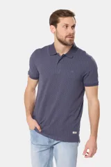 Remera polo de piqué en color azul con estampado de mini print geométrico en toda la prenda. Presenta cuello clásico, cierre frontal con botones personalizados y logo bordado en el pecho.