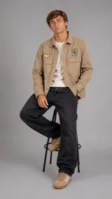 Sobrecamisa de estilo militar en color beige, con cierre frontal de botones, dos bolsillos frontales con solapa y parches decorativos en el pecho.