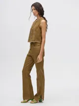 Pantalón de denim color marrón, de tiro alto y calce ochentoso con terminación estilo oxford. Cuenta con apliques metálicos decorativos alrededor de los bolsillos y a lo largo de las costuras exteriores.
