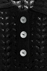 Polo negro de punto calado con cuello clásico, manga corta abullonada y terminación ondulada en el ruedo.