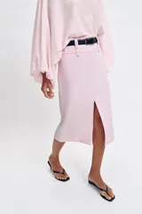 Falda midi tubo de color rosado con abertura frontal en el bajo y cierre lateral con cremallera oculta. Incluye un cinturón negro con hebilla dorada.