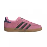 Championes adidas Gazelle Indoor de gamuza en color rosado con las icónicas tres tiras laterales en negro. Presenta un diseño clásico de perfil bajo con suela de goma translúcida y detalle en el talón en color azul oscuro.