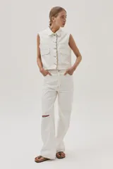 Chaleco de denim blanco con costuras en contraste color ocre, cuello camisero, cierre frontal con botones, bolsillos de parche con solapa en el pecho y sisas desflecadas.
