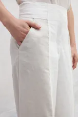 Pantalón de lino color beige y blanco, de corte amplio a la cintura y con bolsillos laterales.