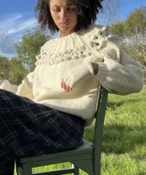 Sweater artesanal de punto en color marfil, confeccionado en pura lana merino. Presenta un amplio canesú decorado con trenzas, bodoques y calados, de mangas largas abullonadas y cuello redondo.