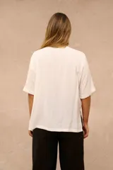 Blusa blanca de corte holgado con cuello redondo, mangas cortas con vuelta y un bolsillo aplicado en el pecho.