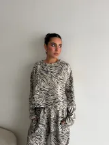 Conjunto de dos piezas compuesto por una remera de manga larga y un pantalón de corte ancho, ambos confeccionados en tela de viscosa con estampado animal print tipo cebra en tonos beige y negro.