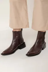 Bota tipo chelsea de caña media con acabado efecto cocodrilo en color chocolate. Presenta paneles elásticos laterales, puntera cuadrada y taco ancho geométrico.