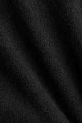 Buzo negro de tejido suave con lana, cuello redondo acanalado, hombros caídos y mangas largas. Puños y bajo en punto acanalado.