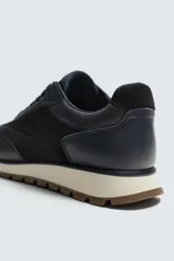 Zapatilla deportiva color verde militar, con parte superior de múltiples piezas que combinan piel y serraje. Presenta horma redonda y suela dentada en color crema con base marrón.