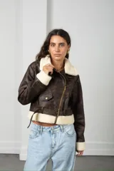 Chaqueta estilo aviador de cuero sintético en tono marrón desgastado, con cuello, puños y ruedo forrados en corderito sintético color crema. Presenta cierre frontal cruzado, bolsillos con solapa y cinturón ajustable en la cintura.